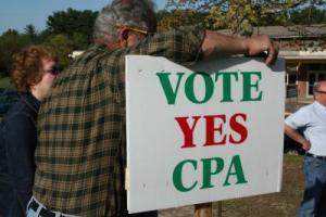 CPA advocates in Hanson lean on a large white sign that reads &quot;Vote Yes CPA&quot;