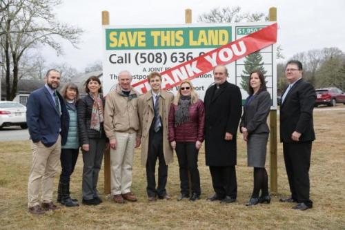A group of advocates in Westport stand in front of a sign charting progress in money raised to save the St. Vincent de Paul land. A large red banner reading "thank you" is hung across the sign