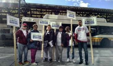 A group of CPA advocates and supports in Boston stand together, all holding signs that read "Yes on 5 For A Better Boston"